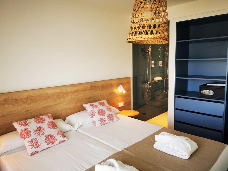 Ein Schlafzimmer mit zwei Einzelbetten, Holzkopfteil, bunten Kissen, Regal und geflochtener Lampe.