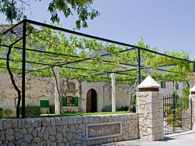 Steinmauer und Pergola vor einem historischen Gebäude mit grünen Fenstern und Türen.