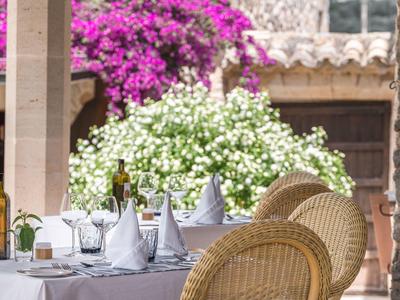 Nakryty stół z butelkami wina i kieliszkami na tarasie z kwiatami w tle.