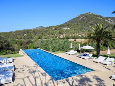 Długi, wąski basen z leżakami i parasolami na tle zalesionych wzgórz pod czystym niebem.