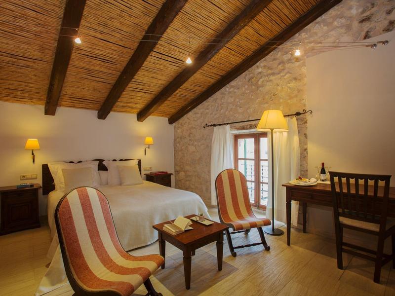 Przytulny pokój hotelowy z drewnianym sufitem, podwójnym łóżkiem, fotelami i biurkiem.