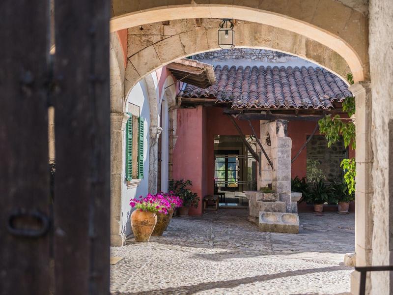 Widok przez łuk na dziedziniec z fontanną i kwiatową dekoracją.