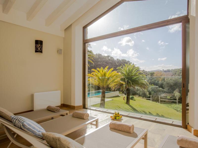 Salon z dużymi oknami z widokiem na ogród z palmami i wzgórzami.