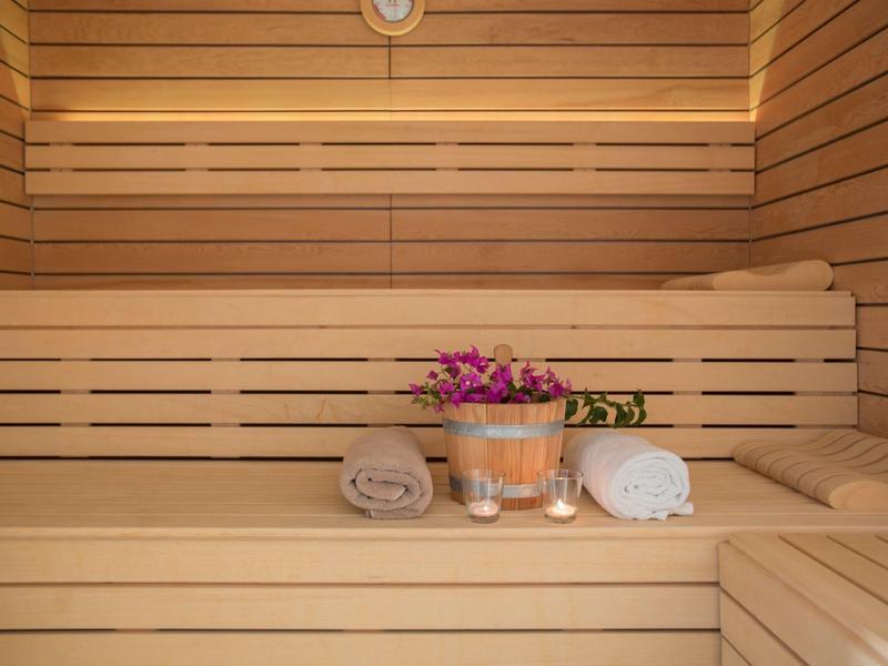 Jasna drewniana sauna z ręcznikami i doniczką z fioletowymi kwiatami.