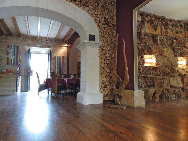 Světle pokoj s dřevěnou podlahou, kamennou zdí a obloukem vedoucím do jídelny se židlemi.