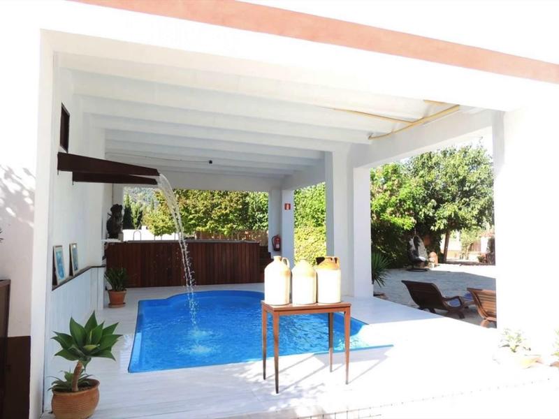 Moderní bazénová oblast s bílou pergolou, stolem se svíčkami a posezením na zahradě.