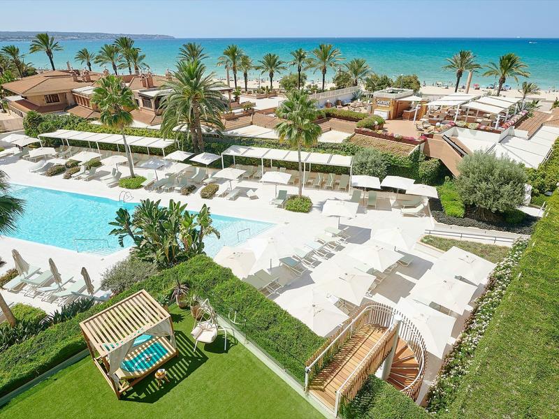 Luxuriöse Strandresort mit großem Pool, weißen Liegestühlen, Palmen und türkisfarbenem Meer im Hintergrund.