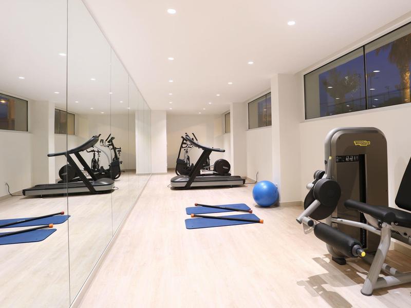 Heller Fitnessraum mit Spiegelwand, Laufbändern, Trainingsgerät, blauer Matte und Gymnastikball.