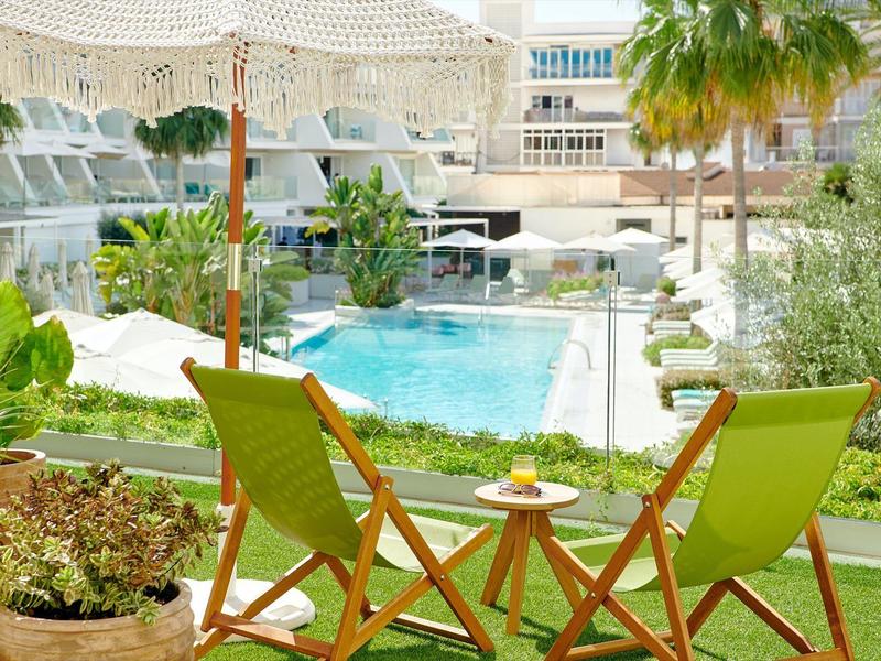 Zwei grüne Liegestühle und ein Tisch mit Getränken am Pool in einem Hotelgarten.