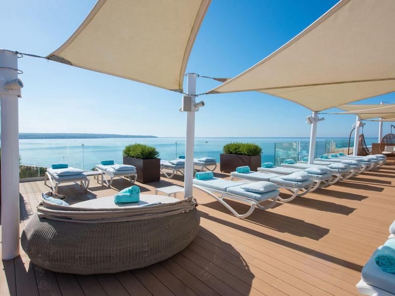 Sonnenterasse mit Liegen und Blick auf das Meer bei klarem Himmel.