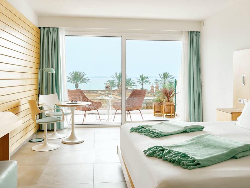 Modernes Schlafzimmer mit großem Fenster, Sandfarbenem Boden, Holzwand und Balkon mit Pflanzen.