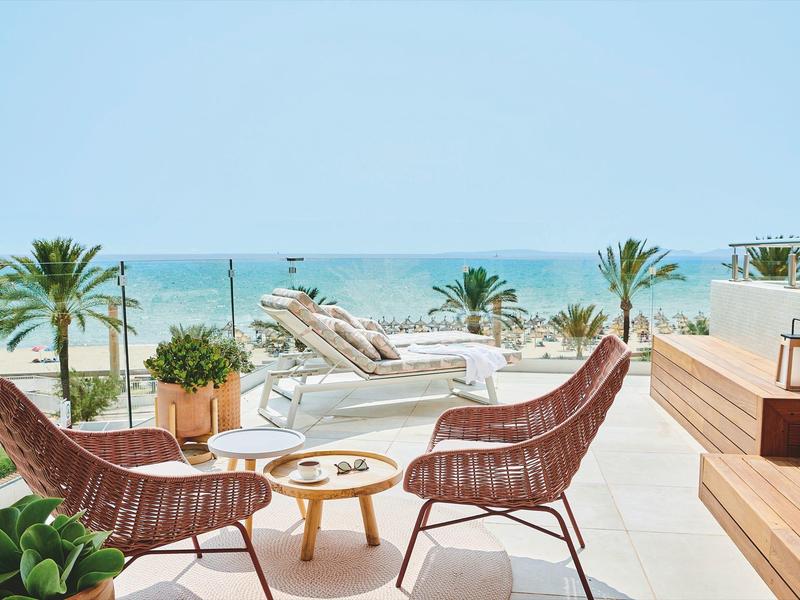 Terrasse mit zwei roten Korbsesseln, kleinem Holztisch, Palmen und Blick aufs blaue Meer.