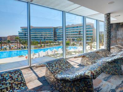 Area relax con lettini curvi e grande parete di vetro con vista sulla piscina esterna.