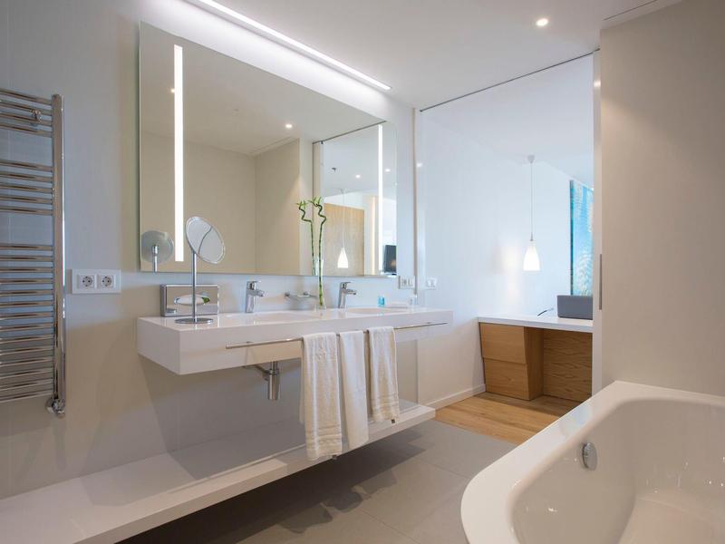 Bagno moderno e luminoso con grande specchio illuminato, doppi lavandini e vasca da bagno.
