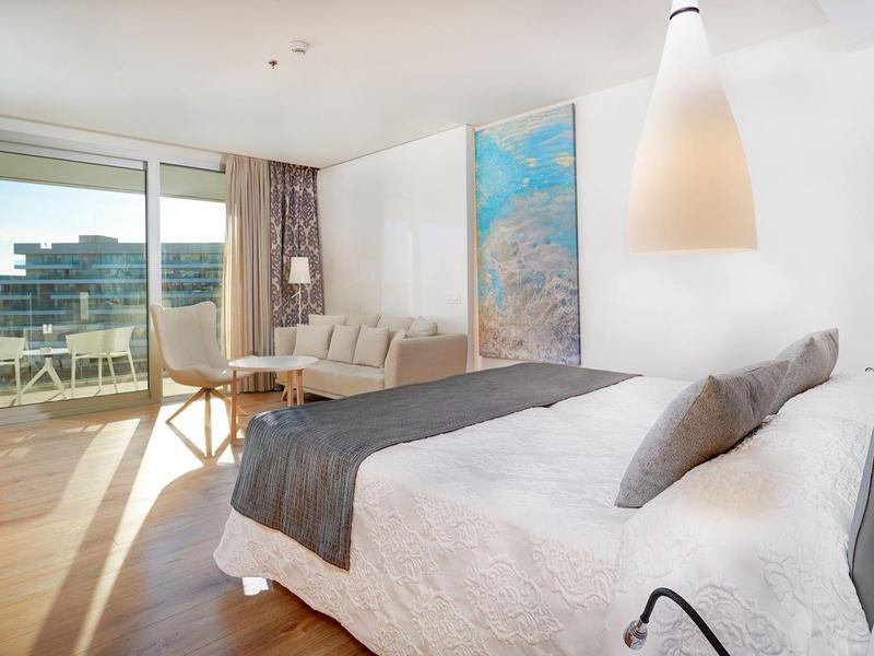 Camera d'hotel moderna con letto grande, zona soggiorno e balcone con vista.