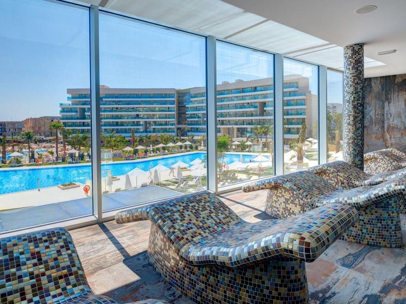 Area relax con lettini curvi e grande parete di vetro con vista sulla piscina esterna.