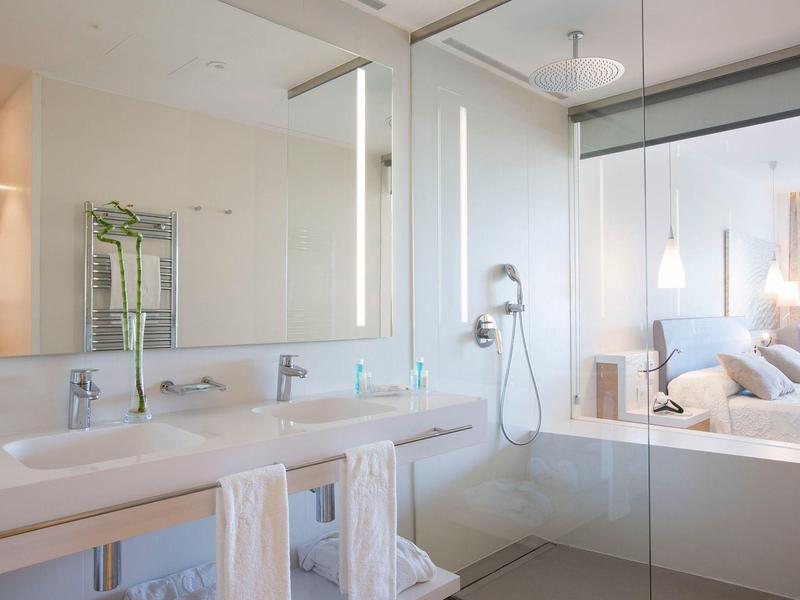 Bagno d'hotel moderno con doppi lavandini, doccia in vetro e vista sulla camera da letto.