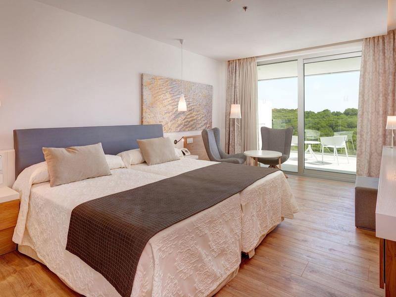 Camera d'hotel moderna con letto matrimoniale, balcone e vista sul verde.