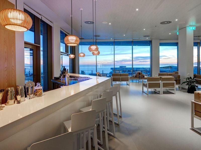 Interno moderno di un bar d'hotel con grandi finestre e tramonto visibile.