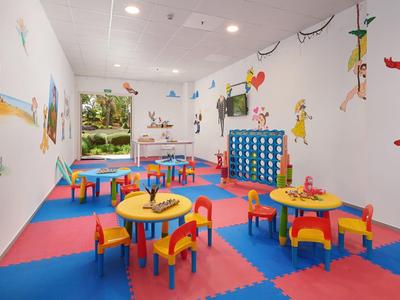Bunter Kinderspielraum mit kleinen Tischen, Stühlen und Comicfiguren an den Wänden.