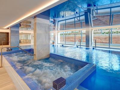 Hallenbad mit Whirlpool, großen Fenstern und modernem Ambiente in Blau- und Beigetönen.