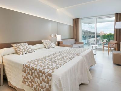 Modernes Hotelzimmer mit zwei Doppelbetten, hellen Wänden, großem Fenster und Balkon mit Aussicht.
