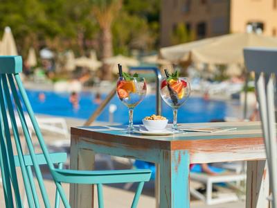 Bunter Holztisch mit Cocktails, Stühlen und Schwimmbad im sonnigen Außenbereich.