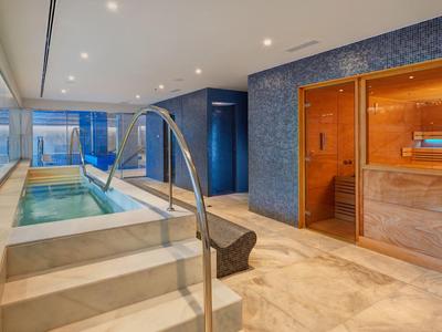 Moderner Wellnessraum mit Sauna, beheiztem Pool und großen Fenstern für Tageslicht.