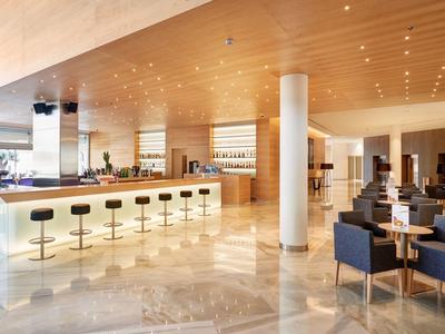 Moderner heller Bar- und Lounge-Bereich mit Holzdecke, Stühlen und Tischen auf glänzendem Boden.
