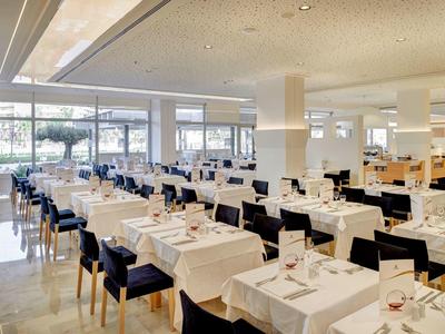 Großer heller Speisesaal mit weiß gedeckten Tischen und schwarzen Stühlen, großes Panoramafenster.