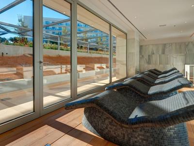 Moderner Raum mit bodentiefen Fenstern, großen Sitzkissen und Blick auf Terrasse mit Pool und Palmen.