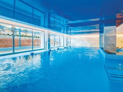 Moderner Innenpool mit klarem blauem Wasser, großen Fenstern und stilvoller Beleuchtung.