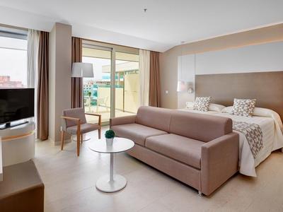 Modernes Hotelzimmer mit großem Bett, Sofa, Flachbildfernseher und Zugang zu Balkon oder Terrasse.