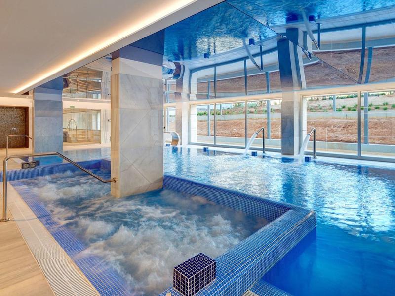 Piscina interna moderna con vasca idromassaggio e grandi vetrate verso l'esterno.