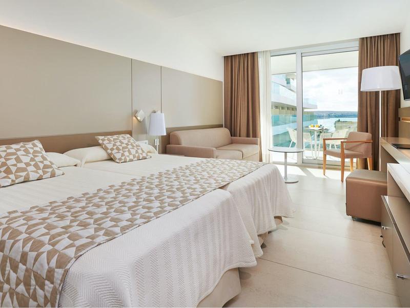 Camera d'hotel luminosa con letto matrimoniale, balcone e arredo moderno beige.