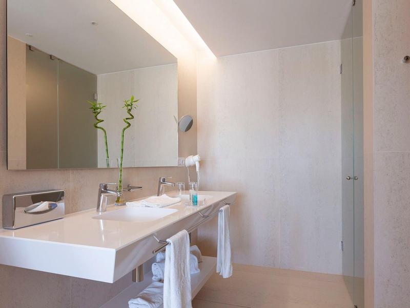 Bagno luminoso con doppio lavandino e due piante verdi accanto allo specchio.