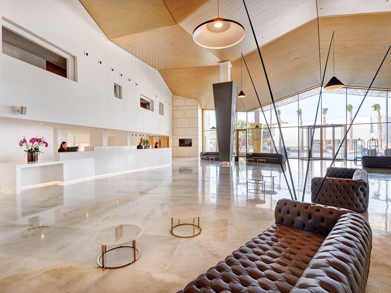 Ampia hall moderna con divano, reception bianca e grandi finestre luminose.