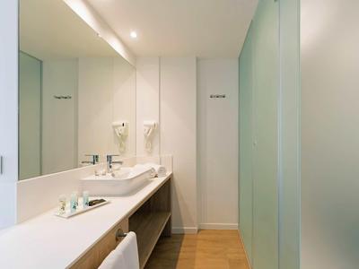 Bright, modern bathroom with a long mirror, white countertop, sink, and glass shower door.