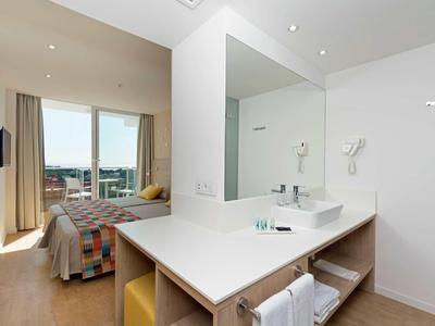 Modern hotel room with large windows, bed, and a sleek bathroom with white walls and towels.