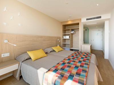Modern hotel room with twin beds, wooden flooring, and colorful bedspread under soft lighting.
