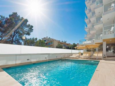 Outdoor pool beside a modern hotel building with clear blue sky and bright sun.