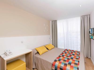 Compact hotel room with double bed, colorful bedspread, desk, and wall-mounted TV.