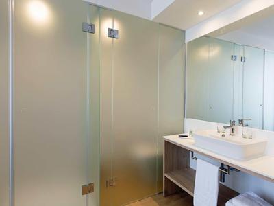 Modern hotel bathroom with frosted glass shower, white sink, large mirror, and clean design.