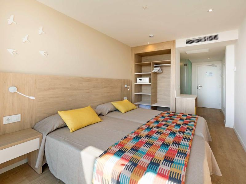 Modern hotel room with twin beds, wooden flooring, and colorful bedspread under soft lighting.