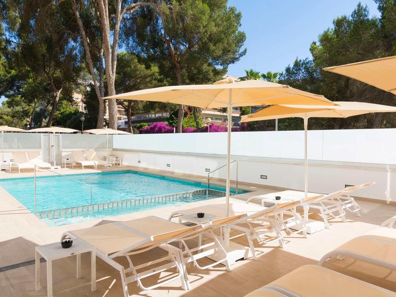 Outdoor pool area with lounge chairs and umbrellas beside a clear swimming pool, surrounded by trees.