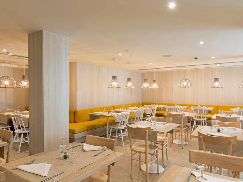 Bright hotel restaurant with wooden tables, yellow bench seating, and modern pendant lamps.