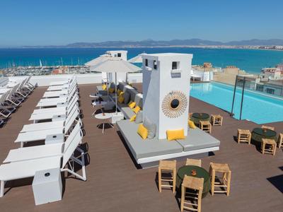 Taras na dachu z basenem, leżakami i stolikami z widokiem na morze przy czystej pogodzie.