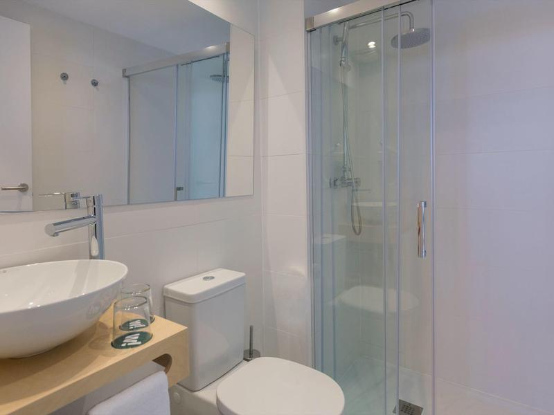 Mała nowoczesna łazienka z okrągłą umywalką, toaletą i kabiną prysznicową z drzwiami szklanymi.