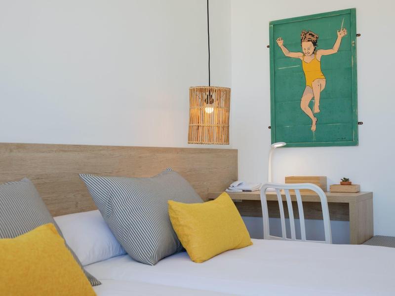 Nowoczesna sypialnia z jasnymi poduszkami i dekoracją ścienną w ciepłych odcieniach.