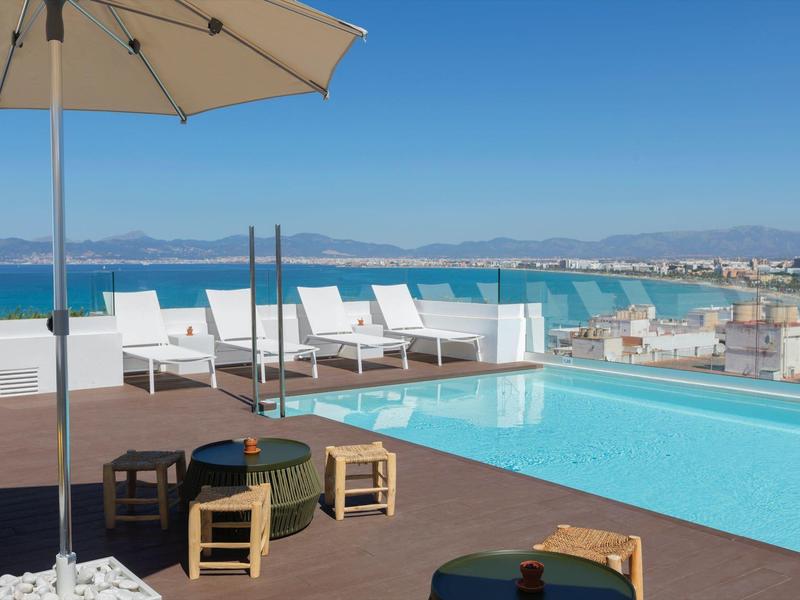Taras na dachu z basenem, leżakami, poduszkami i widokiem na nadmorskie miasto.